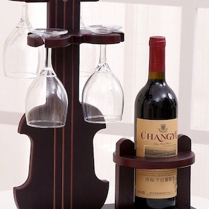 May include: A dark brown wooden wine rack shaped like a violin with four glass holders and a shelf for a bottle of wine. The bottle is labeled "CHANGYU Dry Red Wine" in English and Chinese.