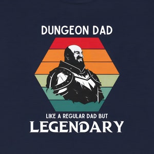 May include: A blue t-shirt with a retro-style graphic of a bearded man in armor. The text "Dungeon Dad" and "Like a regular dad but legendary" is printed on the shirt.