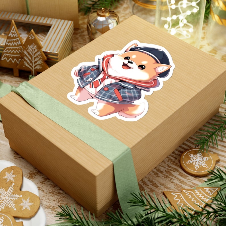 Peut inclure: Un autocollant repr&eacute;sentant un Shiba Inu de dessin anim&eacute; portant une veste en plaid bleu et blanc et une &eacute;charpe ray&eacute;e rouge et blanche. Le chien sourit et porte un chapeau marron sur la t&ecirc;te.