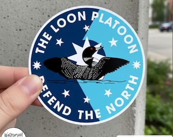 Puede incluir: Una pegatina redonda con una ilustración de un somorgujo, dividida diagonalmente entre azul oscuro y azul claro. El texto dice "THE LOON PLATOON" y "DEFEND THE NORTH". El texto adicional incluye "STICKER/MAGNET" y "Waterproof & Dishwasher Sale".