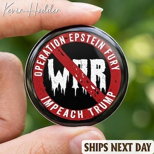 May include: A round black button with the text "OPERATION EPSTEIN FURY" in a red circle, with a red line through the word "WAR" in white, and the words "IMPEACH TRUMP" in white. The button is held between fingers.