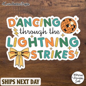 May include: A sticker with the text "Dancing through the Lightning Strikes" in teal, orange, and gold glitter lettering. A disco ball and bow are also featured. The sticker is waterproof and dishwasher safe.