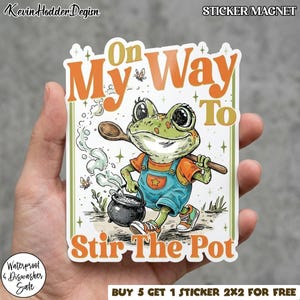 May include: A sticker featuring a cartoon frog in overalls, holding a wooden spoon and stirring a pot. Text reads "On My Way To Stir The Pot." The sticker is green, orange, and blue, with the words "STICKER/MAGNET" at the top.