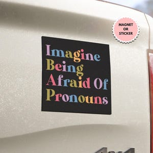 May include: A black square sticker with the text "Imagine Being Afraid Of Pronouns" in colorful letters. The sticker is on a white car.
