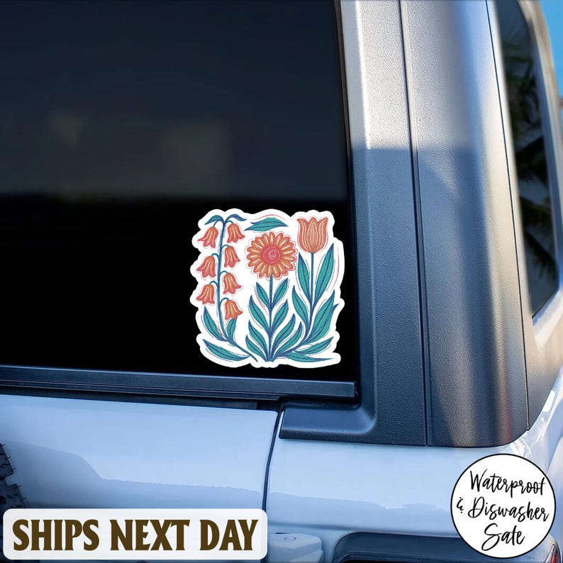 May include: A floral sticker featuring a stylized design of various flowers in shades of orange, pink, and teal. The sticker is applied to a vehicle window. The sticker has a white border. The text "SHIPS NEXT DAY" is at the bottom.