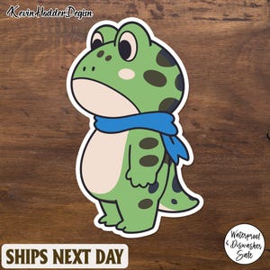May include: A sticker featuring a cartoon frog with a blue scarf. The frog is green with dark green spots and a white belly. The sticker has the text "SHIPS NEXT DAY" at the bottom and "Waterproof & Dishwasher Sale" in a circle.