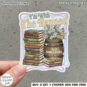 Puede incluir: Una pegatina con el texto "I'm With The Banned" con una pila de libros y un barril de madera lleno de flores. La pegatina también tiene el texto "I Read Banned Books".