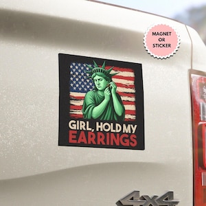 May include: A black square magnet or sticker with an illustration of the Statue of Liberty and the American flag. The text "GIRL, HOLD MY EARRINGS" is in red and white. A pink sticker reads "MAGNET OR STICKER".