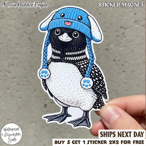 Può includere: Un adesivo o magnete con un fumetto di un colimbo che indossa un cappello invernale blu con paraorecchie e trecce. Il colimbo ha piume nere e bianche. Il testo sull'adesivo recita "Waterproof & Dishwasher Safe" e "Ships Next Day".