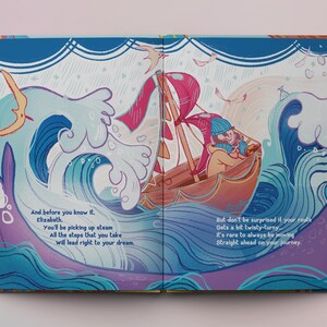 Op de afbeelding: Een open boek met kleurrijke illustraties van een boot die op een blauwe en paarse oceaan met golven vaart. De tekst op de pagina luidt: "En voordat je het weet, Elizabeth. Je zult vaart maken. Alle stappen die je zet, zullen je rechtstreeks naar je droom leiden. Maar wees niet verbaasd als je route een beetje kronkelig wordt. Het is zeldzaam om altijd rechtdoor te gaan op je reis."