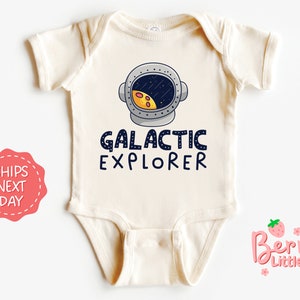 May include: A white baby onesie with a cartoon astronaut helmet and the text "GALACTIC EXPLORER".
