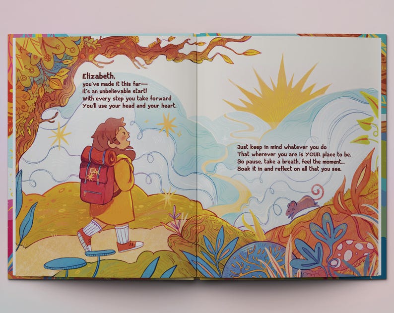 Op de afbeelding: Een ge&iuml;llustreerd boek met een kleurrijke omslag met een jonge persoon met een rugzak die op een pad loopt. De tekst op de pagina luidt "Elizabeth. you've made it this far- It's an unbelievable start! with every step you take forward You'll use your head and your heart. Just keep in mind whatever you do That wherever you are is YOUR place to be. So pause, take a breath, feel the moment... Soak it in and reflect on all that you see."