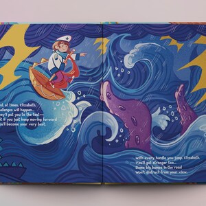 Op de afbeelding: Een open boek met kleurrijke illustraties van een meisje dat op een golf rijdt en een paarse octopus. De tekst luidt "En, soms, Elizabeth, komen er uitdagingen... Ze zullen je op de proef stellen - Maar als je gewoon doorgaat, zul je je best doen." en "met elke hindernis die je overwint, Elizabeth, word je sterker... Sommige grote hobbels op de weg zullen je niet afleiden van je zicht."
