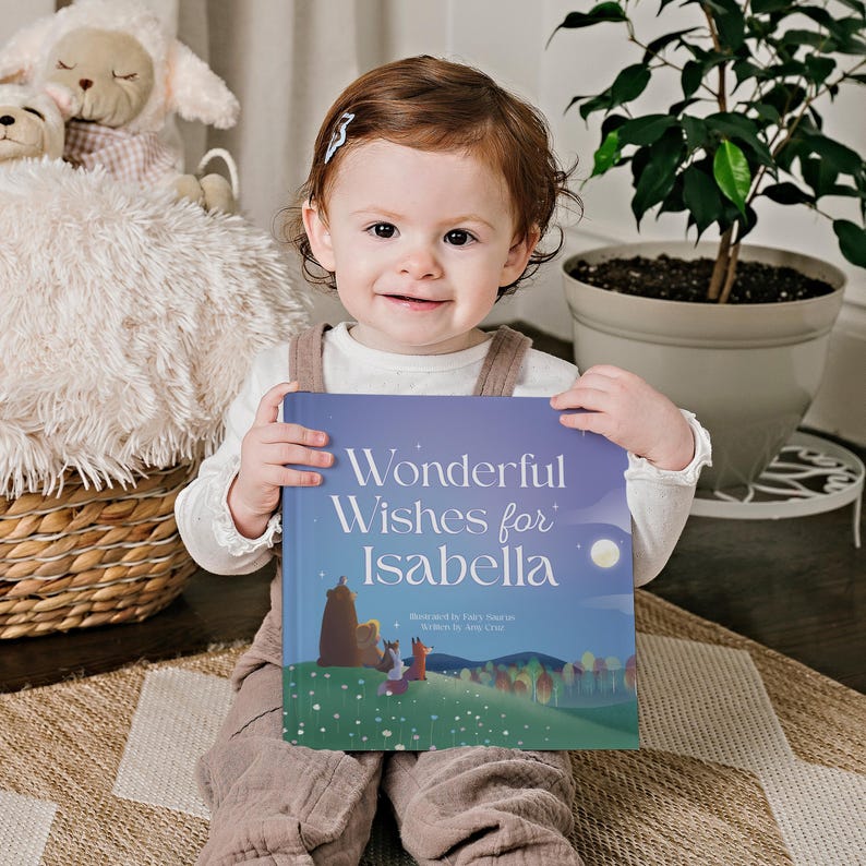 以下が含まれることがあります： 小さな子供が、「Wonderful Wishes for Isabella」というタイトルの青い本を持っています。本には、森の中にいる動物たちのカラフルなイラストが描かれています。