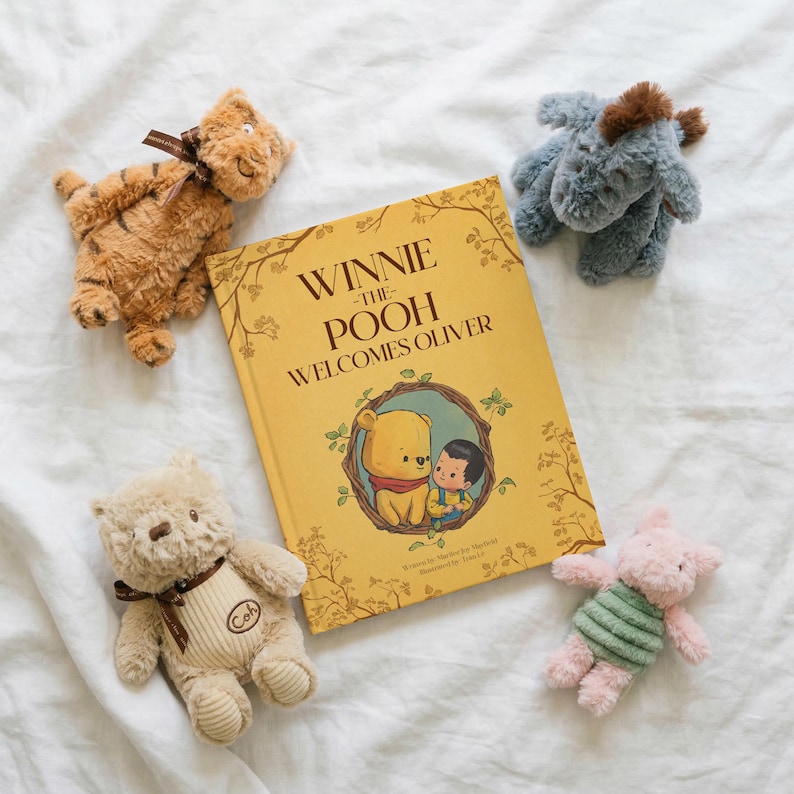 Pode incluir: Um livro infantil intitulado "Winnie the Pooh Welcomes Oliver" est&aacute; rodeado por brinquedos de pel&uacute;cia dos personagens de Winnie the Pooh. Os brinquedos incluem um tigre, um burro, um urso e um porco. O livro e os brinquedos est&atilde;o em uma superf&iacute;cie branca.