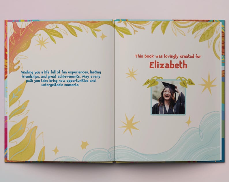Op de afbeelding: Een boek met een kleurrijke omslag met een fantasievolle illustratie van een boom met bladeren en sterren. De tekst op de omslag luidt "Wishing you a life full of fun experiences, lasting friendships, and great achievements. May every path you take bring new opportunities and unforgettable moments." Het boek is open op een pagina met een foto van een vrouw in een afstudeerkap en -jurk. De tekst op deze pagina luidt "This book was lovingly created for Elizabeth."
