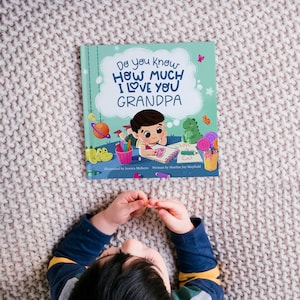 May include: A blue and green children's book with the title "Do you know how much I love you Grandpa". The book features a cartoon illustration of a child drawing a heart on a piece of paper.