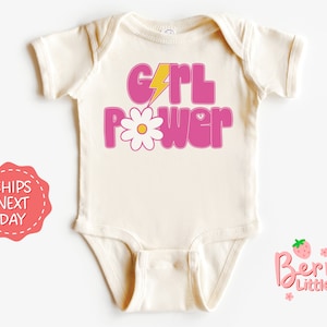 May include: A white baby onesie with a pink and yellow graphic that says "Girl Power" with a daisy and lightning bolt.