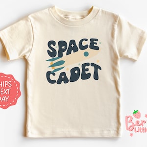 May include: A cream colored short-sleeved t-shirt with the text "SPACE CADET" in a retro font. The text is accompanied by a cartoon rocket ship and stars.