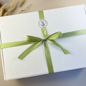 May include: A white gift box with a green ribbon tied in a bow. The box has a sticker with a floral design and the text "Handmade with love and passion".