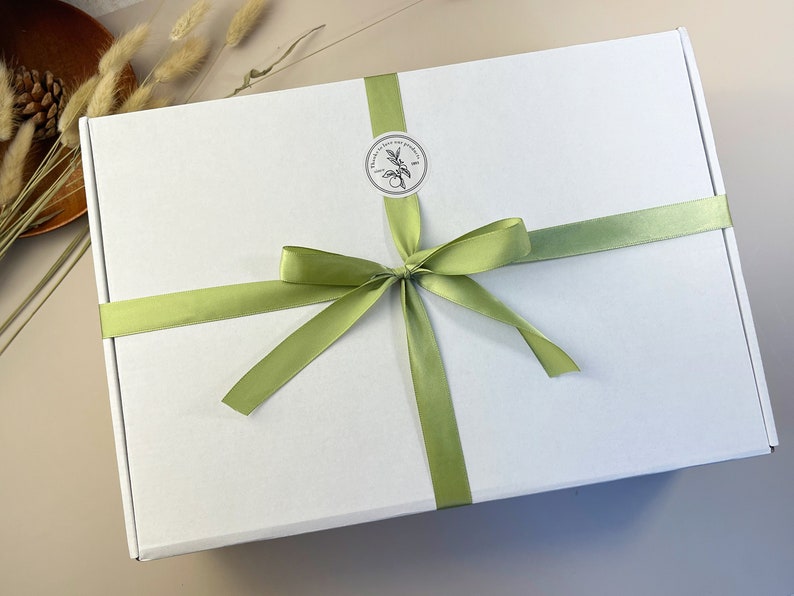 May include: A white gift box with a green ribbon tied in a bow. The box has a sticker with a floral design and the text "Handmade with love and passion".