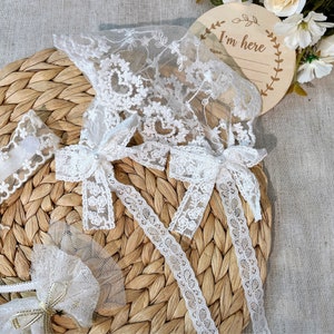 May include: White lace trim with bows and a sign that says "I'm here".