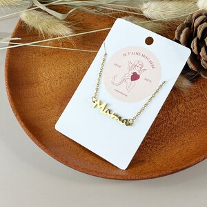 May include: A gold necklace with a cursive "Mama" pendant on a white card with the text "Je t'aime mon b&eacute;b&eacute; since AD 279" and a small illustration of a cherub with a heart.