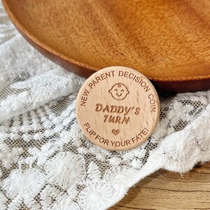 May include: A wooden coin with the text "New Parent Decision Coin" and "Daddy's Turn" with a heart symbol. The coin also says "Flip for your fate!"