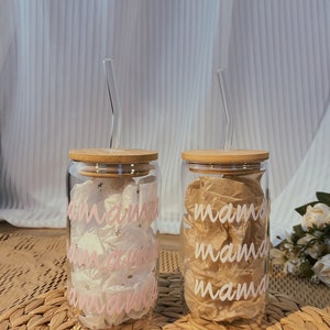 May include: Two glass tumblers with bamboo lids and pink and white straws. The tumblers have the word "mama" written on them in pink and white lettering.