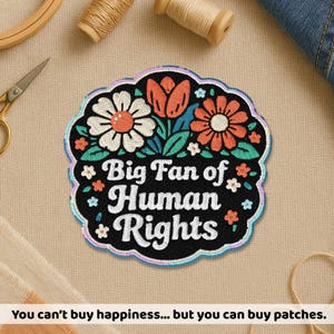 May include: Embroidered patch with the text "Big Fan of Human Rights" in white on a black background. The patch features colorful floral designs in orange, white, and blue. The patch is surrounded by a scalloped edge.