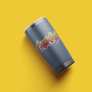 May include: A gray stainless steel tumbler with a colorful graphic of the word "THMAS" in a graffiti style.