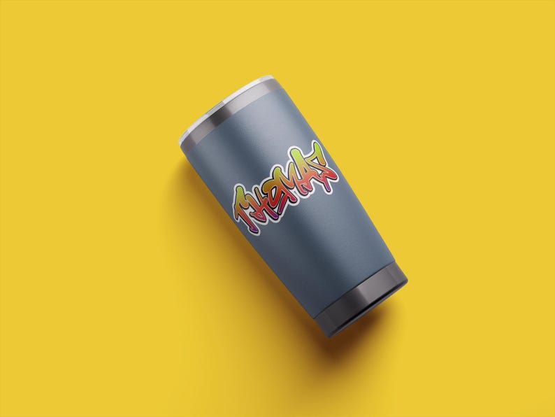 May include: A gray stainless steel tumbler with a colorful graphic of the word "THMAS" in a graffiti style.