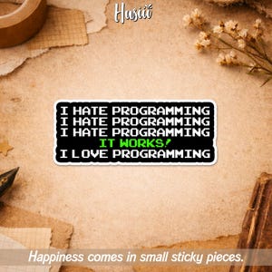 Peut inclure: Un autocollant noir et blanc avec le texte "I HATE PROGRAMMING" répété trois fois, suivi de "IT WORKS!" en vert, et "I LOVE PROGRAMMING". L'autocollant est sur une surface texturée brun clair avec le texte "Happiness comes in small sticky pieces."