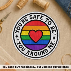 May include: Embroidered patch with a rainbow design and a red heart in the center. The patch has the text "YOU'RE SAFE TO BE AROUND ME." in a circular pattern. The patch is on a beige surface with sewing supplies.