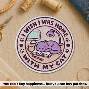 May include: Embroidered patch with the text "I wish I was home with my cat." The design features a purple cat sleeping on a book, a computer, a lamp, and paw prints. The patch is round with a white border.