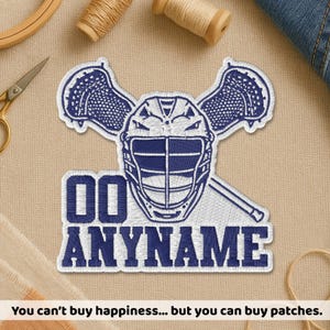 May include: Embroidered patch featuring a lacrosse helmet and sticks in white and navy blue. The patch includes the text "00 ANYNAME" in navy blue. The patch is on a beige background, with sewing supplies visible.