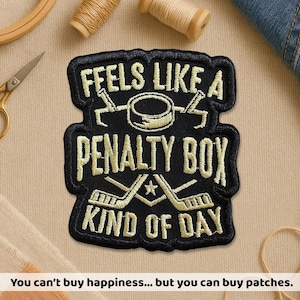 May include: Black embroidered patch with gold text that reads "FEELS LIKE A PENALTY BOX KIND OF DAY." The patch features hockey-themed graphics. The bottom of the image reads "You can't buy happiness... but you can buy patches."
