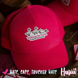 May include: A vibrant pink trucker hat with a mesh back. The hat displays a patch with three cartoon geese and the text "Walking by Faith Tripping Constantly". The image also includes the text "Hats, Caps, Trucker Hats".