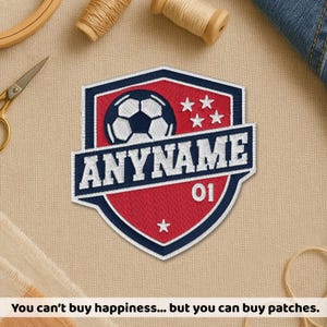 May include: Embroidered soccer patch with a shield design. The patch features a soccer ball, stars, and the text "ANYNAME" in white on a blue and red background. The number "01" is also included.