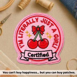 May include: Pink embroidered patch with the text "I'M LITERALLY JUST A GIRL!" and "Certified". Features a red bow and cherries. The patch is surrounded by a pink border and yellow star accents. A fun accessory for clothing or bags.