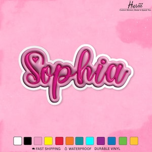 May include: A pink sticker with the name "Sophia" in a 3D script font, outlined in white. A small heart is above the "o". The sticker is on a pink background. The text "Husiii Custom Stickers, Made to Speak You" is in the top right corner.
