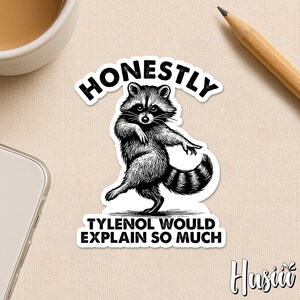 May include: A black and white sticker featuring a raccoon in a dancing pose. The text "HONESTLY" arches above the raccoon, with "TYLENOL WOULD EXPLAIN SO MUCH" below. The sticker has a white border and a signature in the bottom right corner.