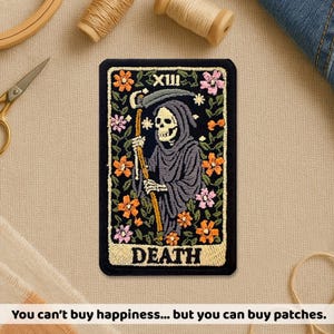 May include: Embroidered patch featuring the Death tarot card. The design includes a hooded skeleton holding a scythe, surrounded by flowers. The text "DEATH" is at the bottom. The patch is rectangular with a black background and floral border.