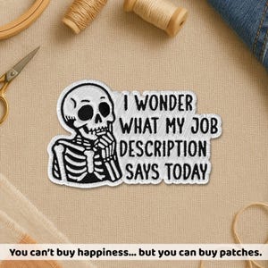Puede incluir: Parche bordado con un esqueleto en blanco y negro y el texto "I WONDER WHAT MY JOB DESCRIPTION SAYS TODAY". El parche está sobre un fondo de tela beige, con suministros de costura visibles. Un artículo humorístico para ropa o accesorios.