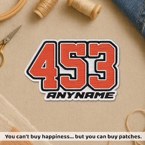 May include: Embroidered patch with the number "453" in orange, outlined in black and white, with "ANYNAME" below. The patch is on a beige fabric surface, with sewing supplies and denim in the background. Text at the bottom reads: "You can't buy happiness... but you can buy patches."