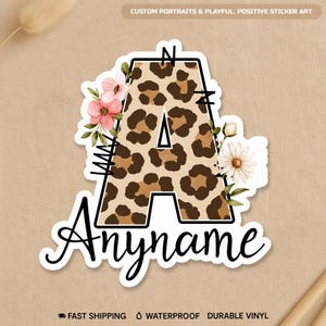 May include: A sticker featuring the letter "A" with a leopard print pattern, outlined in black. The letter is adorned with pink and white flowers and the word "Anyname" in a cursive font. The text "CUSTOM PORTRAITS & PLAYFUL, POSITIVE STICKER ART" is at the top.