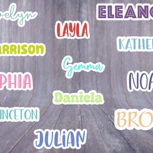 May include: A collection of colorful, personalized name stickers with various names including Eleanor, Layla, Katherine, Sophia, Noah, Brody, Harrison, Evelyn, Gemma, Daniela, Princeton, and Julian. The stickers are on a wood background.