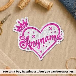 Peut inclure: Écusson brodé en forme de cœur avec une couronne. Le patch est blanc avec des accents roses et le mot "Anyname" en cursive. Le patch est entouré d'une bordure blanche.