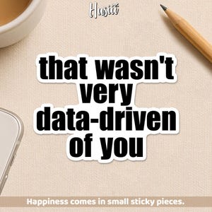 May include: A white sticker with the text "that wasn't very data-driven of you" in a bold, black font. The sticker is on a beige surface, with a pencil and a cup visible in the background. The text "Happiness comes in small sticky pieces" is at the bottom.