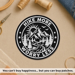 May include: Black and white embroidered patch with the text "HIKE MORE WORRY LESS" around a mountain and forest scene. The patch is round and features stars and birds. The text "You can't buy happiness... but you can buy patches" is at the bottom.